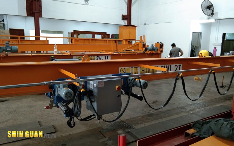 Industrial workshop with overhead cranes and hoist systems being assembled and inspected by a technician